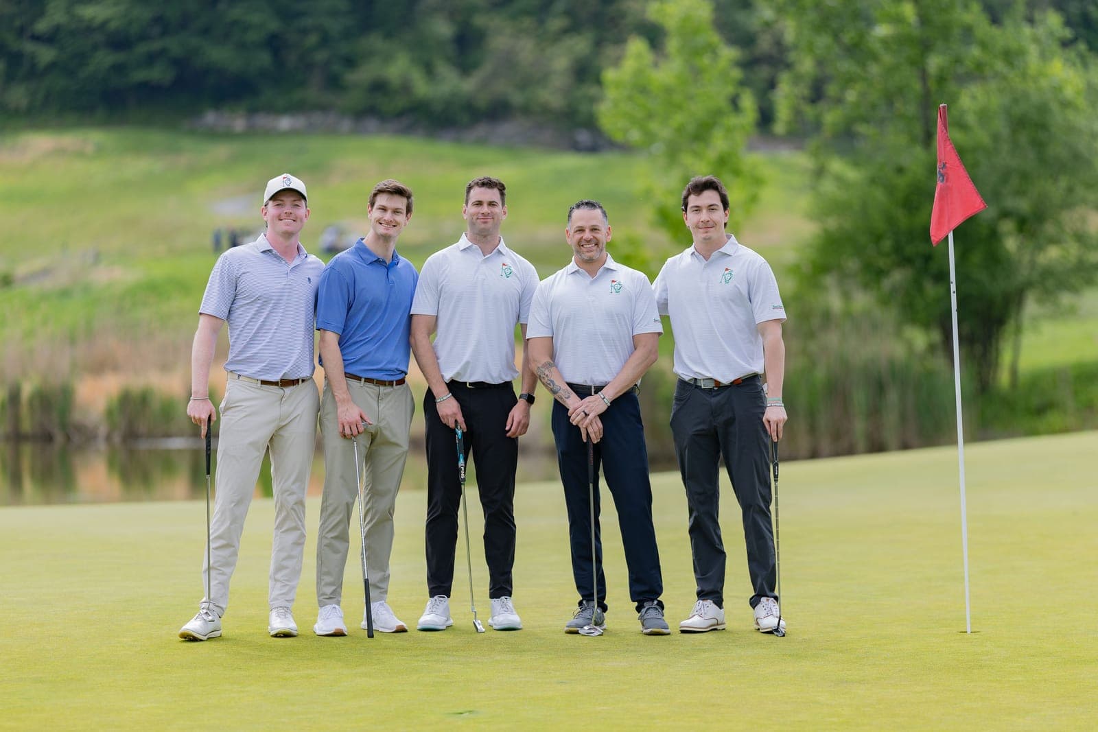 Five golfers with putters standing on the green at the Island Greens Invitational, a red flagstick beside them.